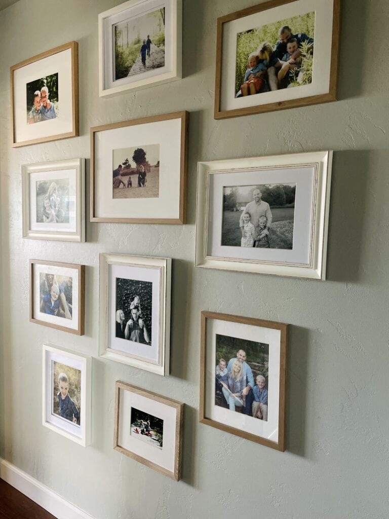 Family photo gallery wall with a mix of white and natural wood frames arranged on a soft green wall.