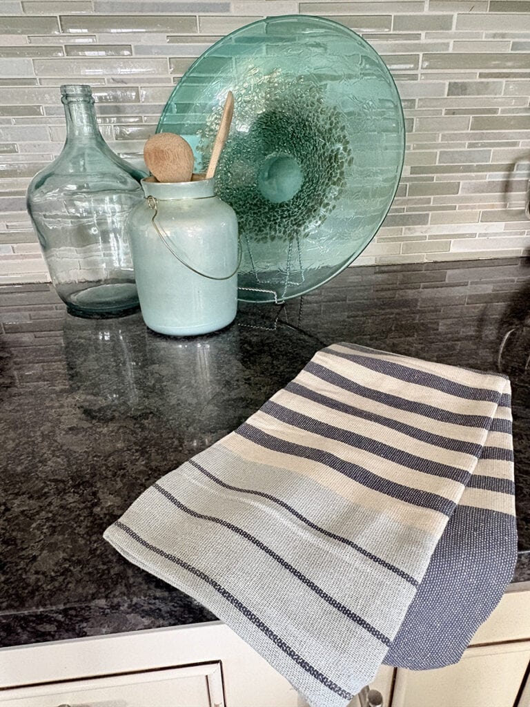 Blue and white striped kitchen towel styled on a kitchen counter with aqua glass decor.