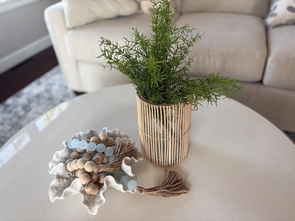 Aqua decorative beads styled in a coral bowl with greenery for coastal coffee table decor.