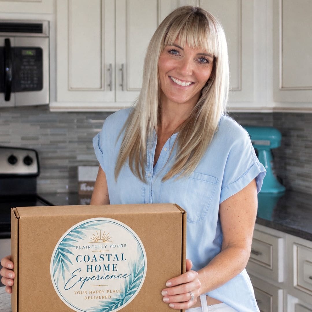 Wendy of Flairfully Yours smiling in her kitchen while holding the Coastal Home Experience subscription box, featuring its signature aqua botanical label and Your Happy Place, Delivered tagline.